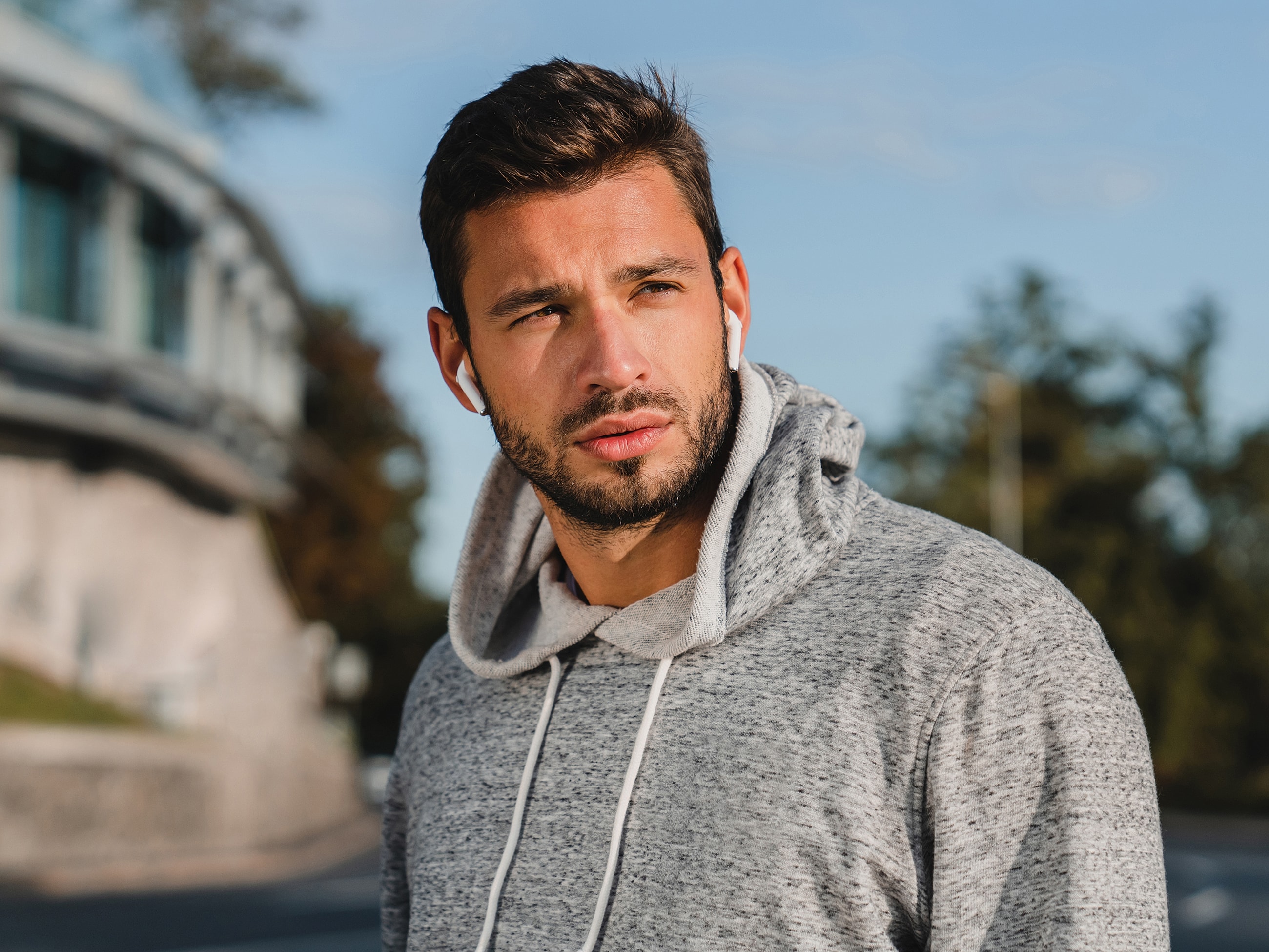 Man wearing earbuds in a hoodie outdoors.